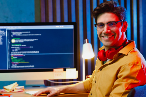 Étudiant ou professionnel souriant en train d'apprendre ou de travailler sur un site web, avec du code affiché sur son écran.